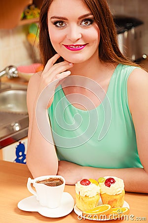 Woman with coffee and cake in kitchen. Gluttony. Stock Photo