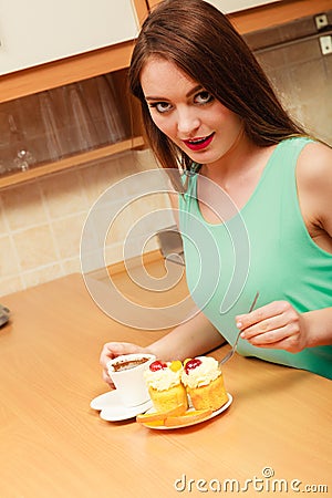 Woman with coffee and cake in kitchen. Gluttony. Stock Photo
