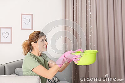 Woman collecting leaking water from ceiling in living room. Stock Photo