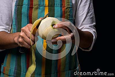 Woman in colored apron peeling apple. Dark black background Stock Photo