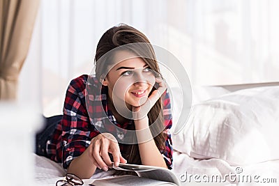 Woman is comfortable lying on her bed with a book, smiling and happy and dreaming Stock Photo