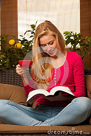 Woman comfortable sitting on sofa, reading book and drinking tea Stock Photo