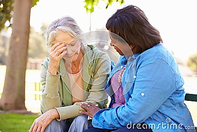 Woman Comforting Unhappy Senior Friend Outdoors Stock Photo