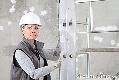 Woman construction worker builder portrait wearing white helmet holding a ladder on interior site building background with Stock Photo