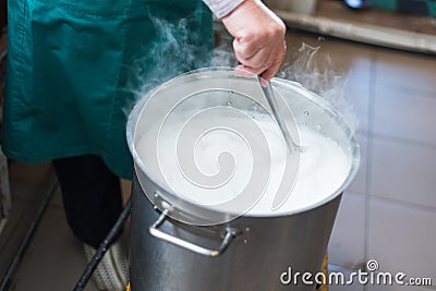 A woman cooks milk in a vat and makes cottage cheese and cheese at home. Production of cheese on the farm Stock Photo