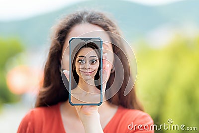 A woman covers her face with a smartphone with a cartoon portrait of a woman. The concept of hiding identity and fake pages in Stock Photo