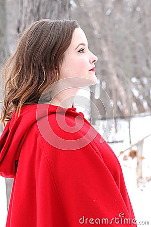 Woman with curly, long hair in vintage red cape looks forward in outdoor winter scene Stock Photo