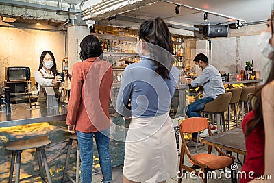 Woman customer receiving food from waitress with face mask on counter then next customer come and order food by social distancing Stock Photo