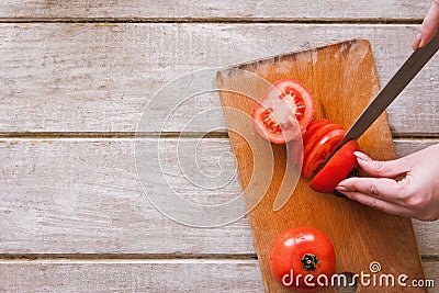 Woman cuts red tomato on parts on wooden desk Stock Photo