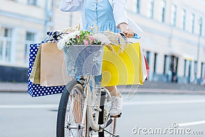 Woman is cycling on white bicycle with packages on handlebars Stock Photo