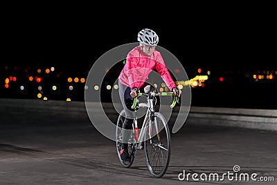 Woman Cyclist Riding Road Bike at Night in the City. Healthy Lifestyle and Urban Sport Concept Stock Photo