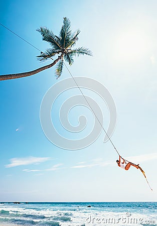Woman dangles on tropical palm tree swing over ocean waves Stock Photo