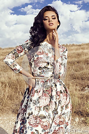 Woman with dark hair wears luxurious colorful dress posing in summer field Stock Photo