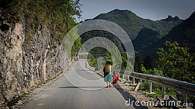 Woman with daughter in traditional vietnamese clothes with a basket behind her back walking on the road Editorial Stock Photo