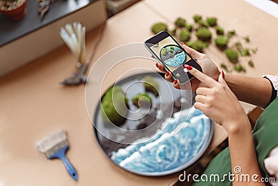 Woman decorator making photo of green ikebana on tray with epoxy resin in florist workshop Stock Photo