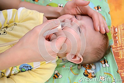 The woman deletes slime from a nose to the sick crying baby with a nasal aspirator Stock Photo