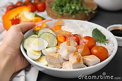 Woman with delicious poke bowl at black wooden table, closeup Stock Photo