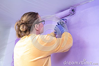 Woman designer paints wall with a roller in color very peri renovates cozy home Stock Photo