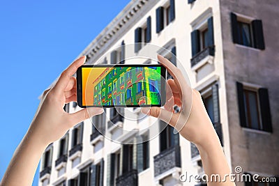 Woman detecting heat loss in building using thermal viewer on smartphone. Energy efficiency Stock Photo