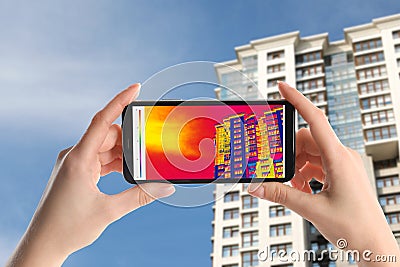 Woman detecting heat loss in building using thermal viewer on smartphone. Energy efficiency Stock Photo