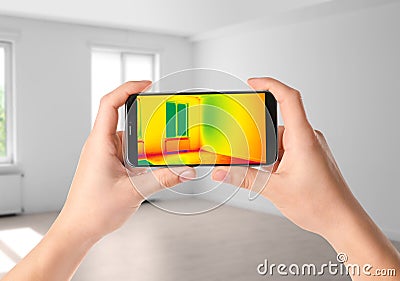 Woman detecting heat loss in room using thermal viewer on smartphone Stock Photo