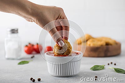 A woman dips a slice of chicken nuggets in ketchup on a light background. Stock Photo