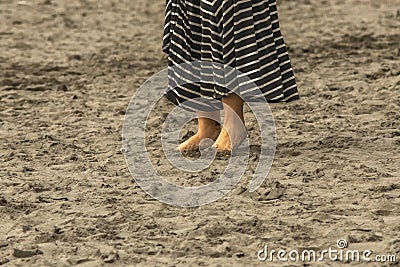 Woman with dirty feet and toes dug into the sand on the beach with longish dress - bottom one third of body - close-up and Stock Photo