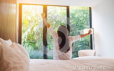 A woman do stretching after waking up in the morning , looking at a beautiful nature view outside bedroom Stock Photo