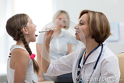 Woman doctor examining little girl mouth at office. Doctor at hospital checking the sore throat of a young patient Stock Photo