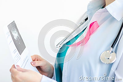 Woman doctor with pink ribbon on white medical uniform holds results of ultrasound scan in her hands. Breast cancer Stock Photo
