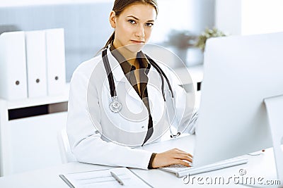 Woman-doctor typing on pc computer while sitting at the desk in hospital office. Physician at work Stock Photo