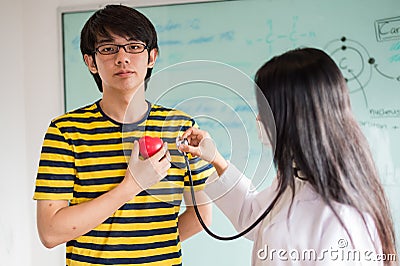 Woman doctor using stethoscope listen heart beat sound from red heart plastic on hand of patient. Stock Photo