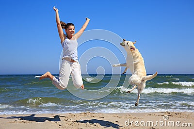 Woman and dog breed Labrador jumping on the beach Stock Photo