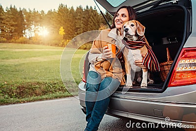 Woman and dog with shawls sits together in car trunk on autumn Stock Photo