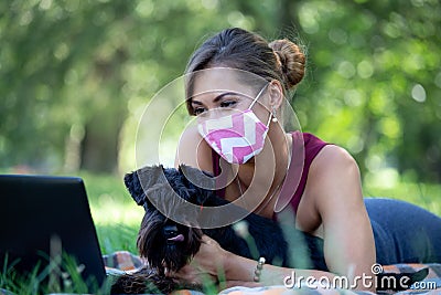 Woman with dog wearing mask and working on laptop in park Stock Photo