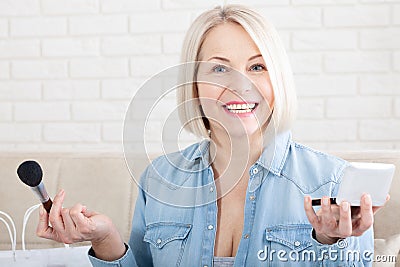 A woman's delicate hands and face in profile expertly adorning her face with makeup, as she prepares Stock Photo