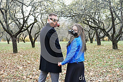 A woman with dreadlocks and a gas mask holds the hand of a man with steampunk goggles and a gas mask. Love in an Stock Photo