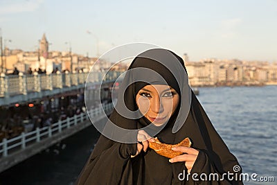 Woman dressed black headscarf, chador eating simit, istanbul, turkey Stock Photo