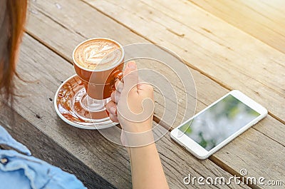 A woman drinking coffee and using phone on wood table Stock Photo