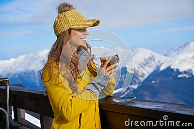 Woman drinking warm tea in the rustick wooden terrace on mountain, alpine view, snow on hills Stock Photo