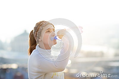 Woman drinking water during a running. Cold weather. Jogging woman in a city during a winter. Sunny day. Drinking mode. Stock Photo