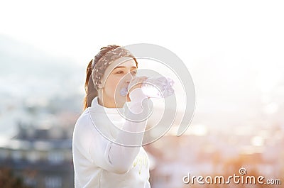 Woman drinking water during a running. Cold weather. Jogging woman in a city during a winter. Sunny day. Drinking mode. Stock Photo