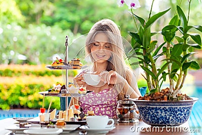 Woman drinks coffee or tea cup with desserts in outdoor restaurant Stock Photo