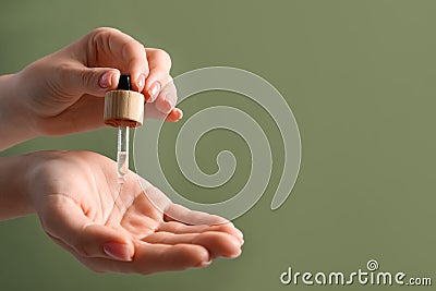 Woman dripping serum from pipette on her hand against olive background, closeup. Space for text Stock Photo