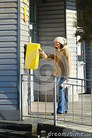 Woman dropping letter into yellow postal box Stock Photo