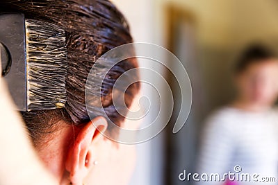 Woman dying her hair with brush in front of mirror in her own bathroom Stock Photo