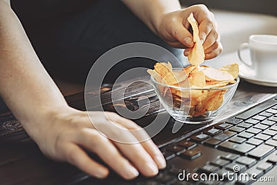 Woman eating chips from bowl at her workplace Stock Photo