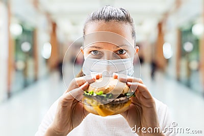 Woman Eating Fastfood Burger In Face Mask Stock Photo