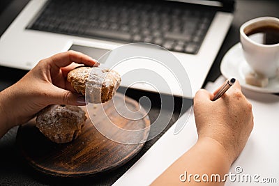 Woman eating muffin at workplace. Unhealthy snack Stock Photo