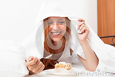 Woman eating sweet cake under sheet in bed Stock Photo